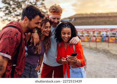 A young group of friends are at a festival texting with a friend who is absent on their smartphone. - Powered by Shutterstock