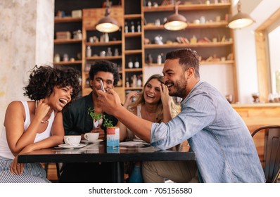 Young group of friends sitting in a cafe and using mobile phone. Young man and women sitting at cafe table and laughing. - Powered by Shutterstock