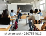 Young group of gen z students attending class at high school. Young black student boy asking a question to senior female teacher during lecture. Education concept