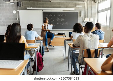 Young group of gen z students attending class at high school. Young black student boy asking a question to senior female teacher during lecture. Education concept