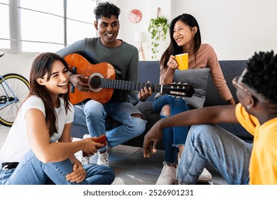 Young group of millennial people having fun together at modern flat. Happy indian man playing the guitar enjoying time with his friends at home