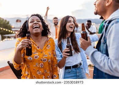 Young group of people dancing together at rooftop party. Diverse friends having fun drinking beer while celebrating birthday at home terrace. - Powered by Shutterstock