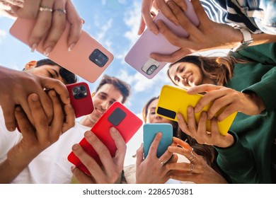 Young group of people using mobile phone device standing together in circle outdoors. Millennial friends addicted to social media app, betting or playing video game on platform online. - Powered by Shutterstock