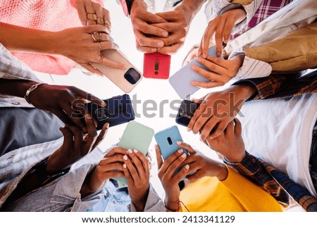Young group of student people using smartphone together outside. Addicted millennial friends using cell phone at city street. Low angle view.