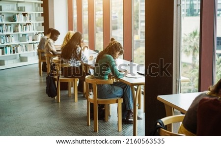 Young group of students studying together inside university library - Focus on center girl hand