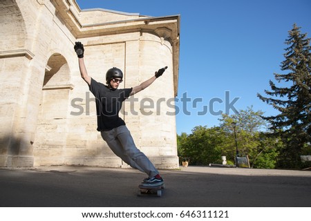 A young guy action makes a stand-up slide on a longboard in the resort area of the city