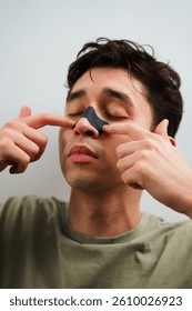Hombre joven que aplica la tira de la nariz del carbón para la limpieza profunda de los poros de la nariz. Concepto de belleza masculina y cuidado de la piel