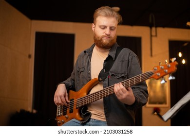 A young guy with a beard plays a bass guitar with five strings - Powered by Shutterstock