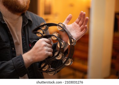 A young guy with a beard plays the tambourine