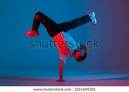 young guy dancer break dancing in neon red blue lighting, active energetic man doing acrobatic tricks, crazy moves and dancer poses