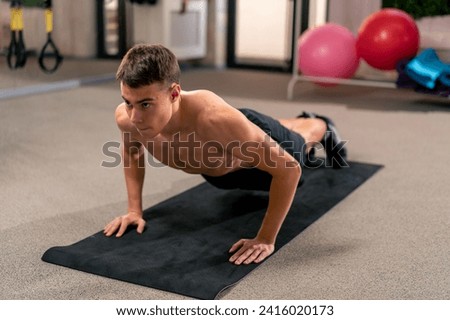 young guy doing push-ups on the mat in the gym doing exercises for the muscles of arms