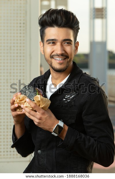 Young\
guy is eating a burger. Outside. selective\
focus
