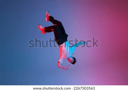 young guy falls upside down in the air, man levitates and flies down in neon lighting, acrobat dancer flies in a jump, concept of dreams and fantasies