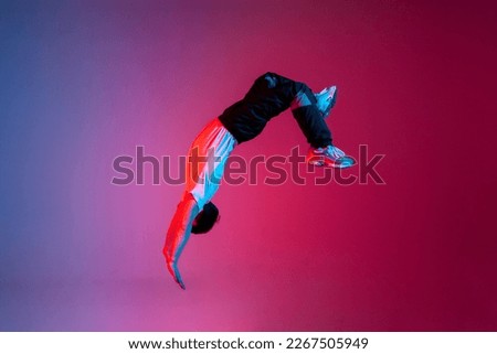 young guy falls upside down in the air, man levitates and flies down in neon lighting, acrobat dancer flies in a jump, concept of dreams and fantasies