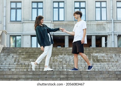 young guy and a girl on the street. the guy holds the girl's hand, and they take a step towards each other.