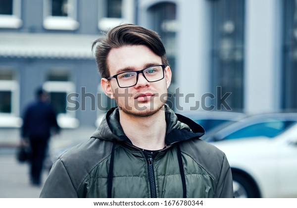 Young guy in glasses and a jacket on a city\
street near the\
building\
