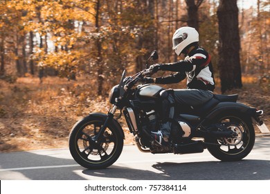 A Young Guy In A Helmet Is Riding On A Forest Road On An Electric Motorcycle. He Sits Confidently In The Saddle. There Are Green Trees Around Him.