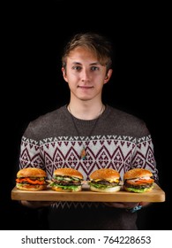 young guy holding a burgers on a wooden tray. black background.