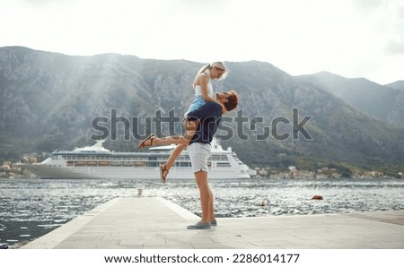 A young guy is holding his girlfriend in arms while they having fun at a holiday on a beautiful day on the seaside together. Love, relationship, holiday, sea