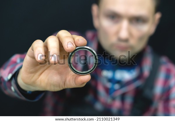 A young guy holds a bearing in his hand on a
black background. A bicycle mechanic in the workshop changes
bearings for the steering column. Repair of motorcycles and cars in
the service center.