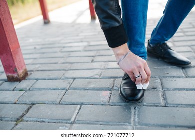 young guy in jeans standing at the bus stop, rubbing the shoes against dirt. closeup: hands and shoes