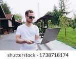 young guy with laptop doing remote work on a sunny day. talk on the telephone. dress up in white t-shirt and black jeans