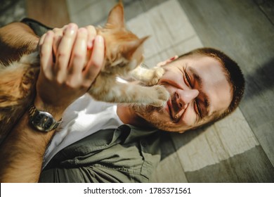 a young guy lies on the floor and hugs maine coon cats. Fun with kittens. Man in white T-shirt holding kitten in hands. male cat lover. the cat touches the man's face - Powered by Shutterstock