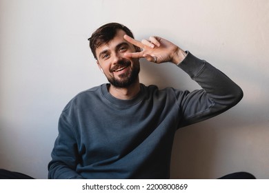 Young Guy Listening To Music Using  Wireless Headphones Doing Peace Symbol With Fingers Over Face, Smiling Cheerful Showing Victory, Have Fun, Dancing.