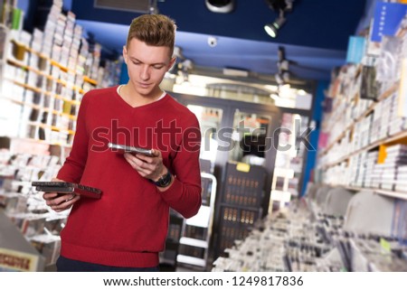 young guy looking on box of DVD movie during shopping in CD shop