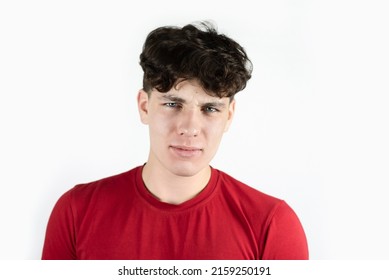 The young guy looks at the camera with suspicion, a grin, doubt. Teenager boy has emotions of doubt, distrust on his face on a light background. Isolated