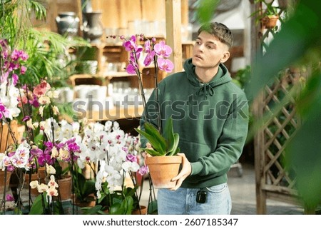 Young guy lovingly selects a flower pot with orchid flowers in a flower shop