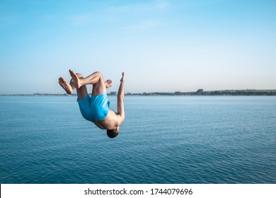 The Young Guy Makes A Jump Back To The Sea. The Man Does A Backflip Into The Water. The Guy Jumps In The Beautiful Blue Sea