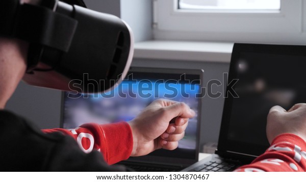 Young guy (male) player in virtual glasses plays\
(relaxes) against him 2 game monitors, he moves his hands seeing\
the movement with glasses. Concept of: Lifestyle, Underworld, 3d,\
Virtual reality