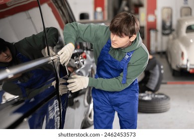 Young guy mechanic in uniform inspects car door in car service station - Powered by Shutterstock