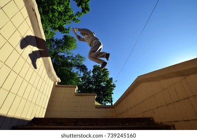 A young guy performs a jump through the space between the concrete parapets. The athlete practices parkour, training in street conditions. Bottom view