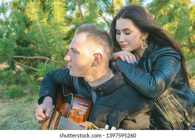 Young Guy Playing Guitar For Her Girlfriend. The Rest Of The Two Young People In The Nature