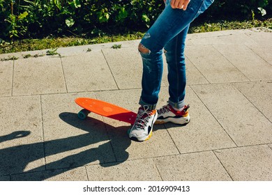 Young Guy In Ripped Jeans Standing With Penny Board In The Park. Summer Activities Skateboarding