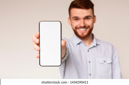 Young guy showing his phone with blank space on camera and smiling, panorama