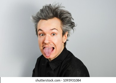 Young Guy Shows Tongue In The Image Of A Physicist Albert Einstein On Gray Background.