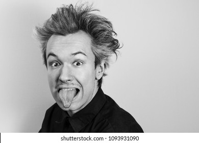 Young Guy Shows Tongue In The Image Of A Physicist Albert Einstein On Gray Background.