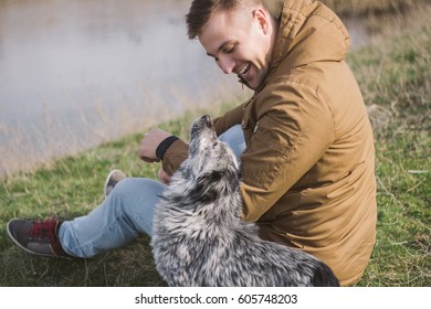 A young guy sits on the river bank with a dog, play, are struck. - Powered by Shutterstock