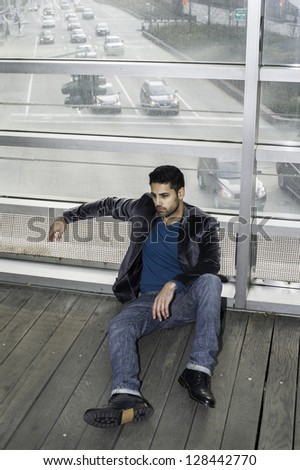 A young guy is sitting on the floor and think. Background is a road on the street and many cars./Cross Road