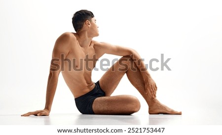 Young guy sitting on floor shirtless, in underwear, demonstrating perfectly, healthy and strong body isolated on white studio background. Concept of male beauty, body and skin care, health, sport