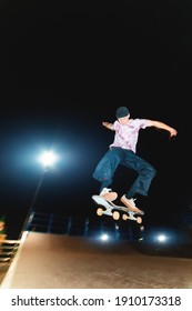 Young Guy Skateboarder Doing A Jump Trick At Night In A Skatepark