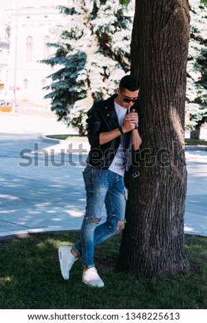a young guy smokes around a tree in the city.bad habit.smoking in a public place