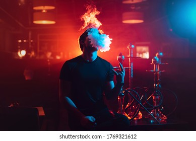 Young Guy Smokes A Shisha And Lets Out A Cloud Of Smoke In The Hookah Room