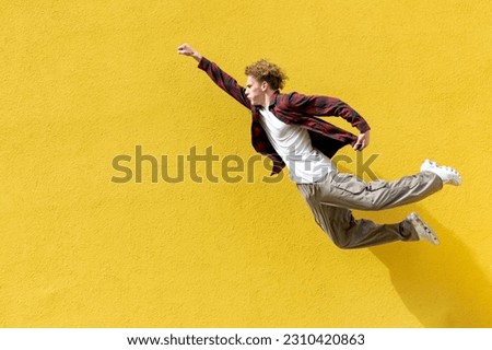 young guy student quickly flies forward in the air against the background of yellow isolated wall, energetic man jumps and hurries