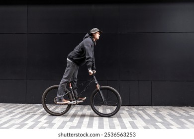 young guy student rides a bike against a black wall, hipster man freestyles on a stunt bike and looks at copy space - Powered by Shutterstock