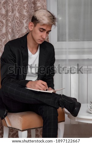 A young guy in a suit writes down his thoughts in a notebook.
