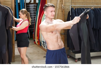 Young guy surfer choosing surfing suit for rent in beach club - Powered by Shutterstock